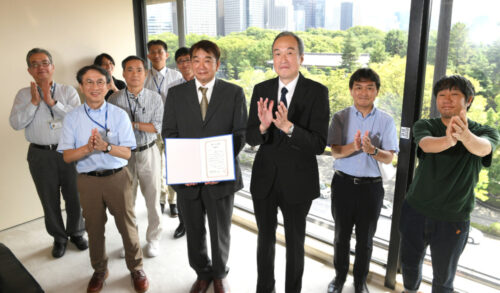  毎日新聞社で飛行１万時間を達成した藤田浩一操縦士（前列左から２人目）。松木健社長（同３人目）による表彰式には、仕事をともにした写真記者や整備士、航空部長らが駆け付けた。