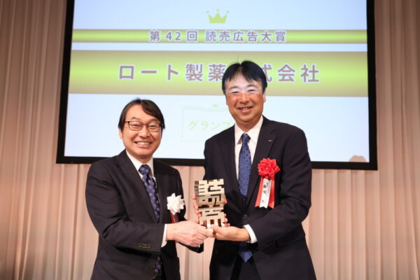  読売新聞東京本社の村岡社長（左）からトロフィーを受け取るロート製薬の梅岡執行役員